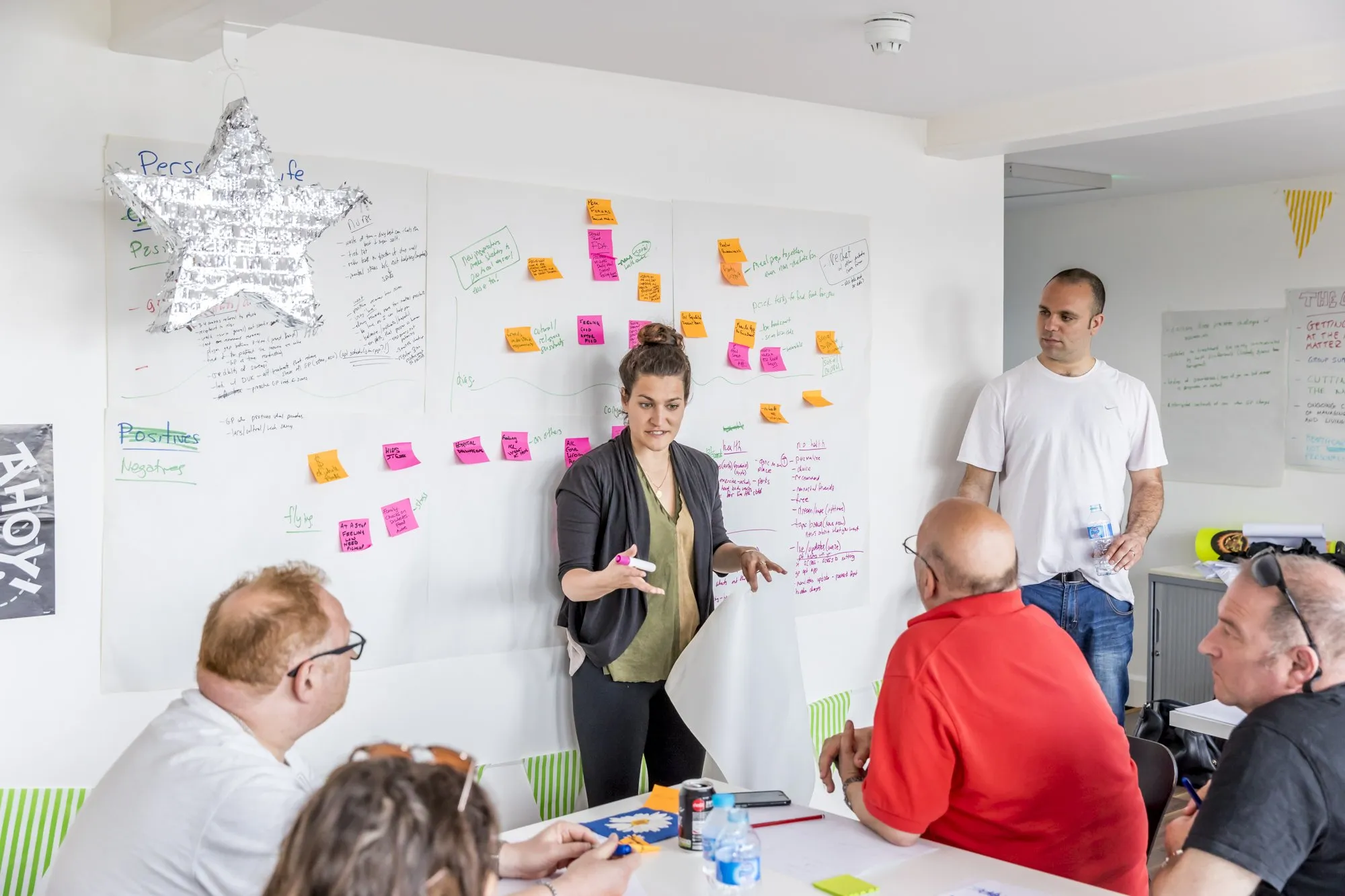 A woman explains the notes on the wall to the group around a table