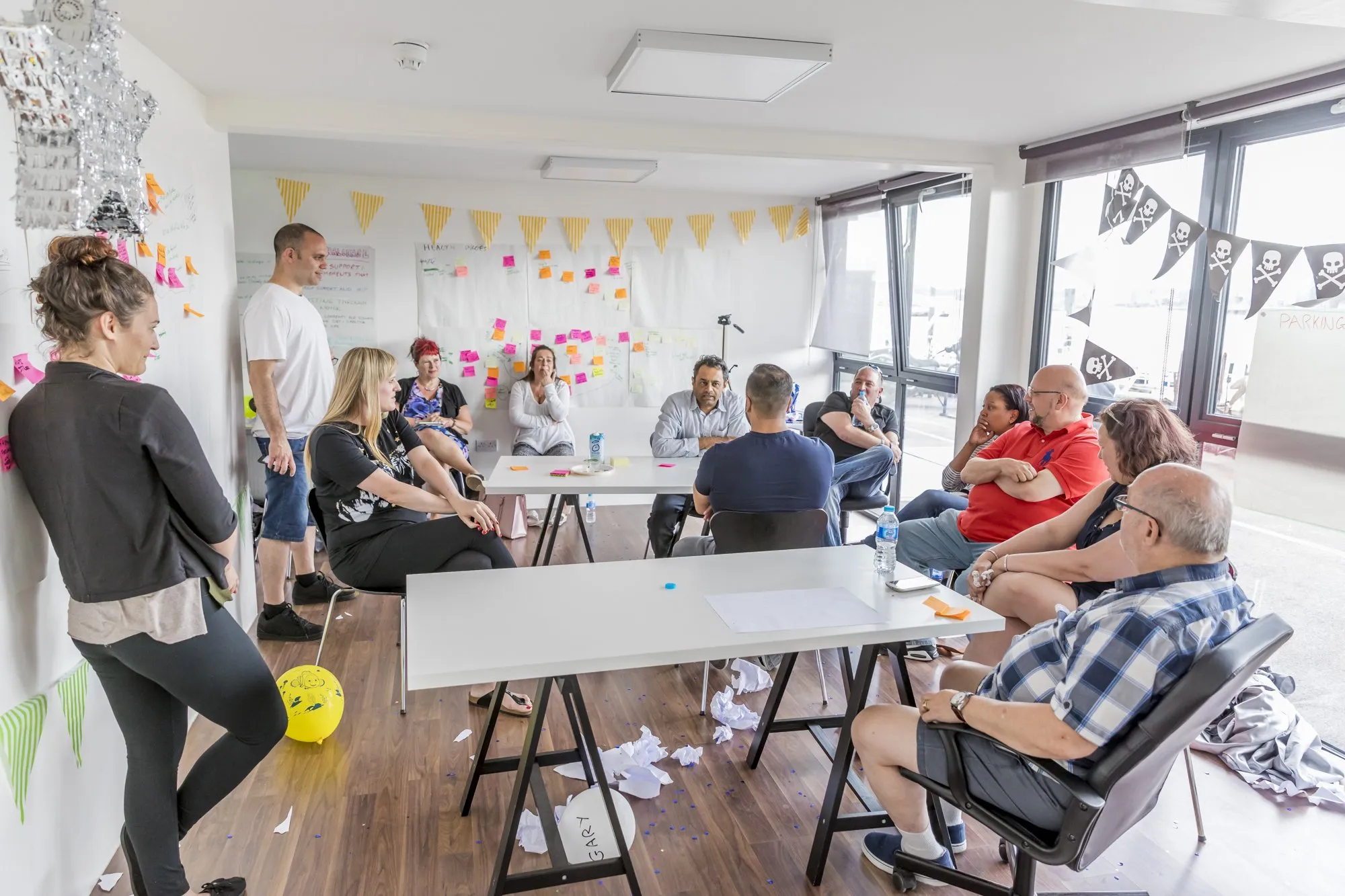 A bright workshop room with bunting, walls of sticky notes and people talking around tables