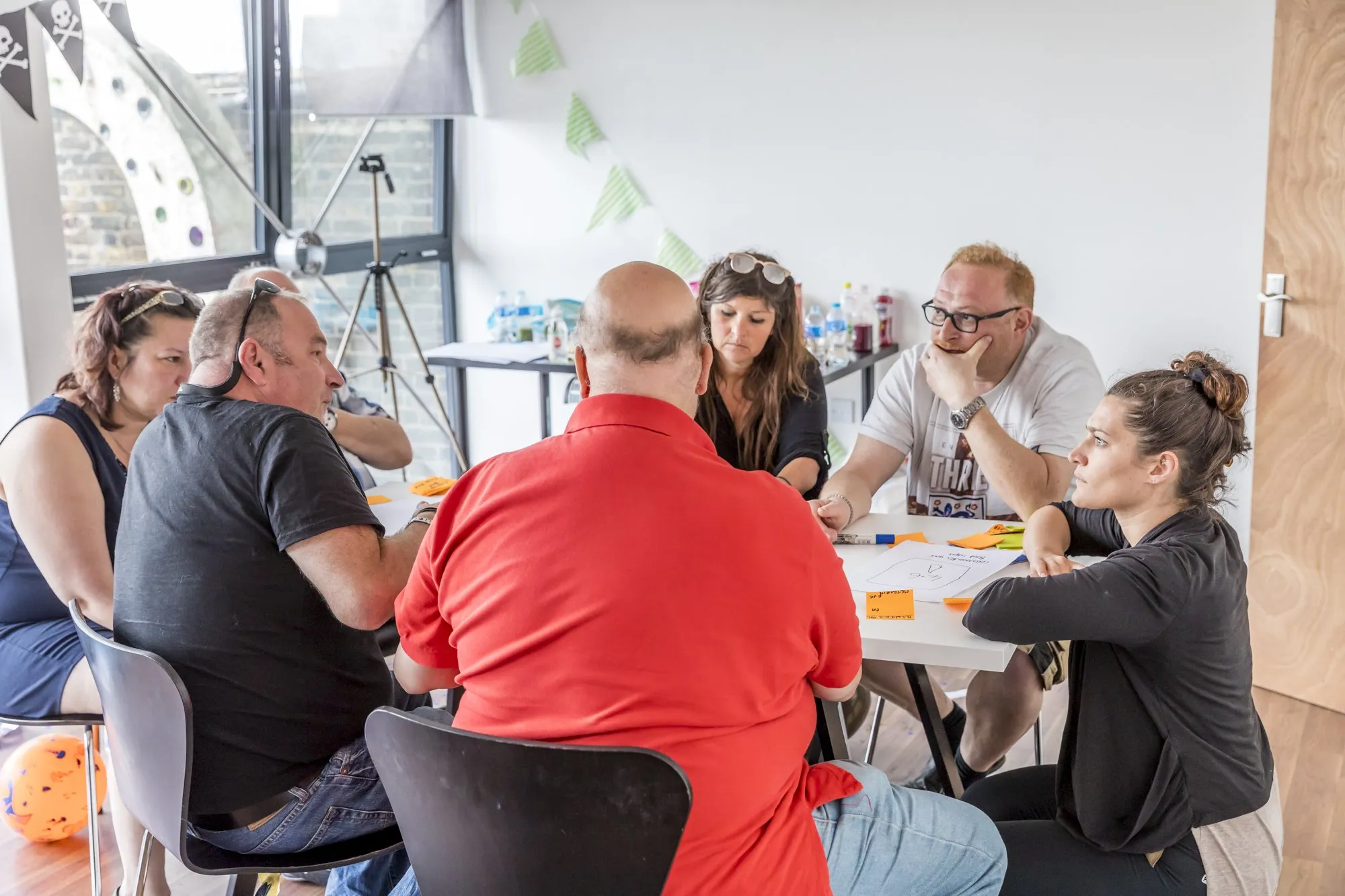 People sit around a table covered in papers and sticky notes, talking things through