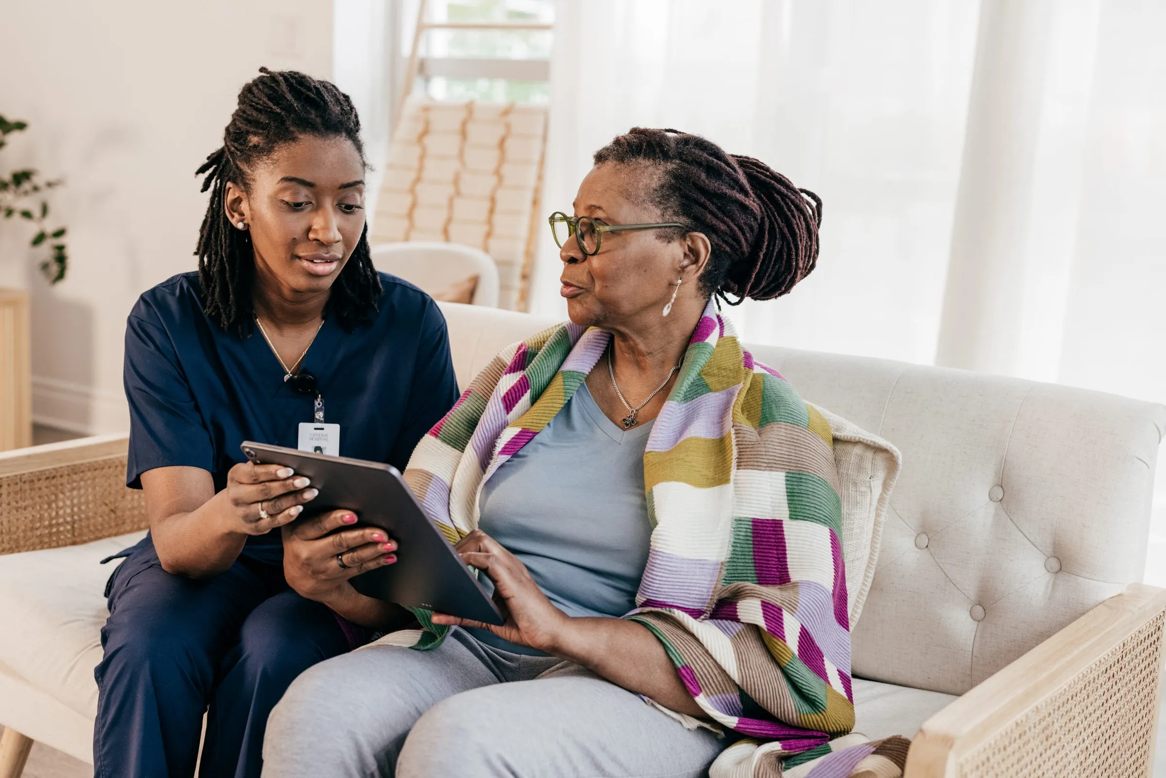 A care worker shows an older woman something on a tablet at home