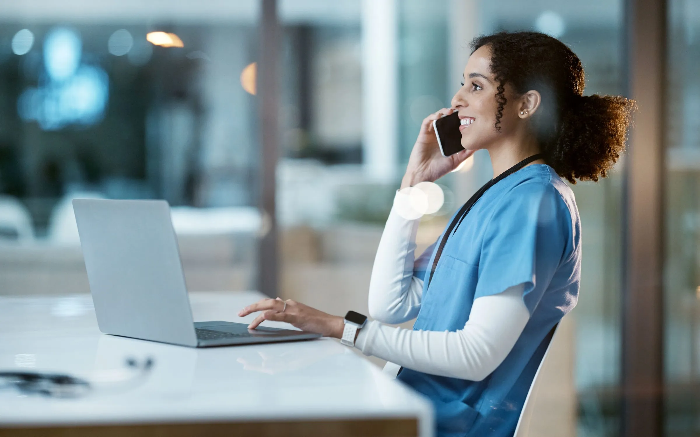 A clinician smiles as she talks on the phone at her laptop