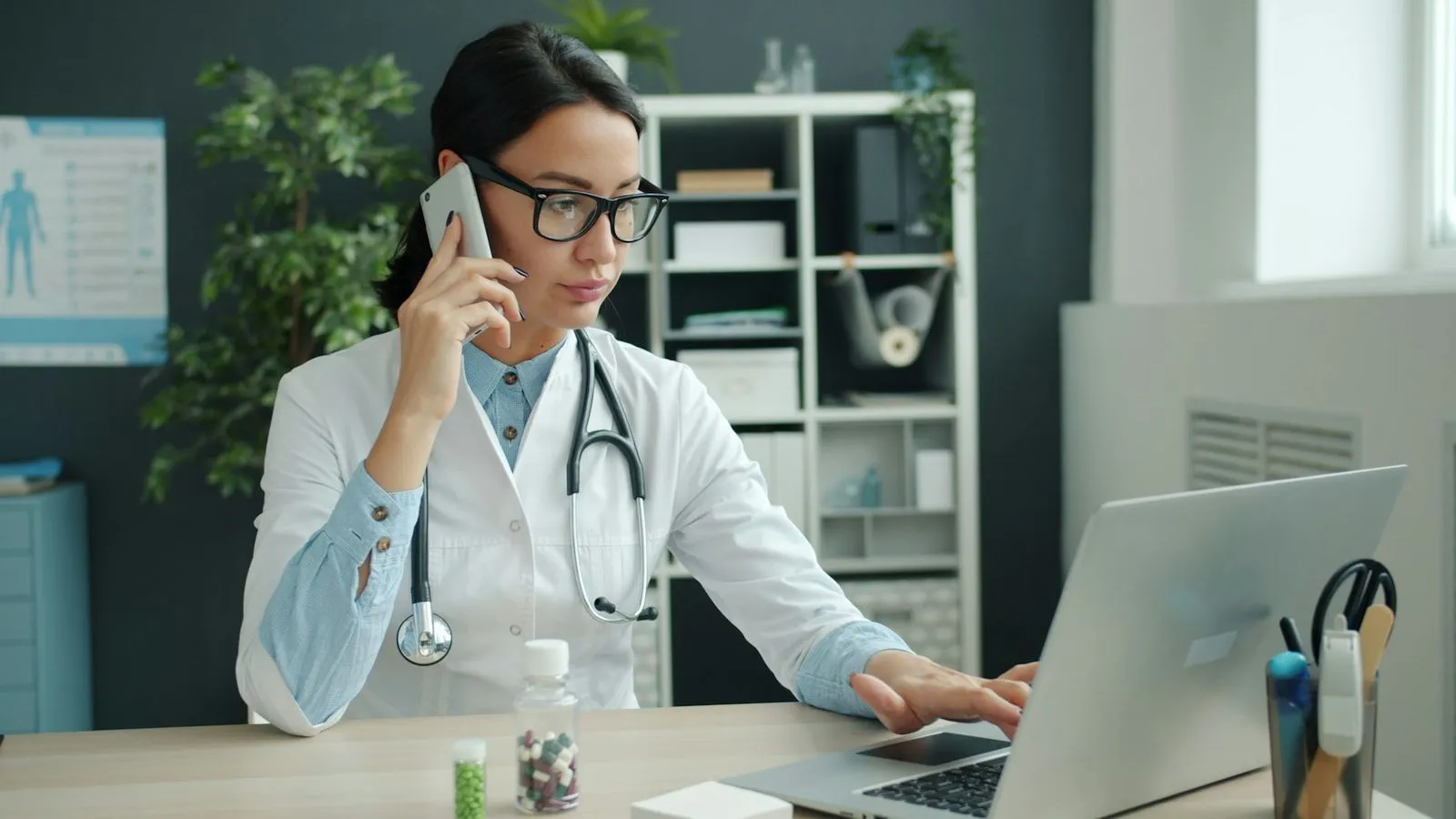 A clinician works at her laptop while on the phone