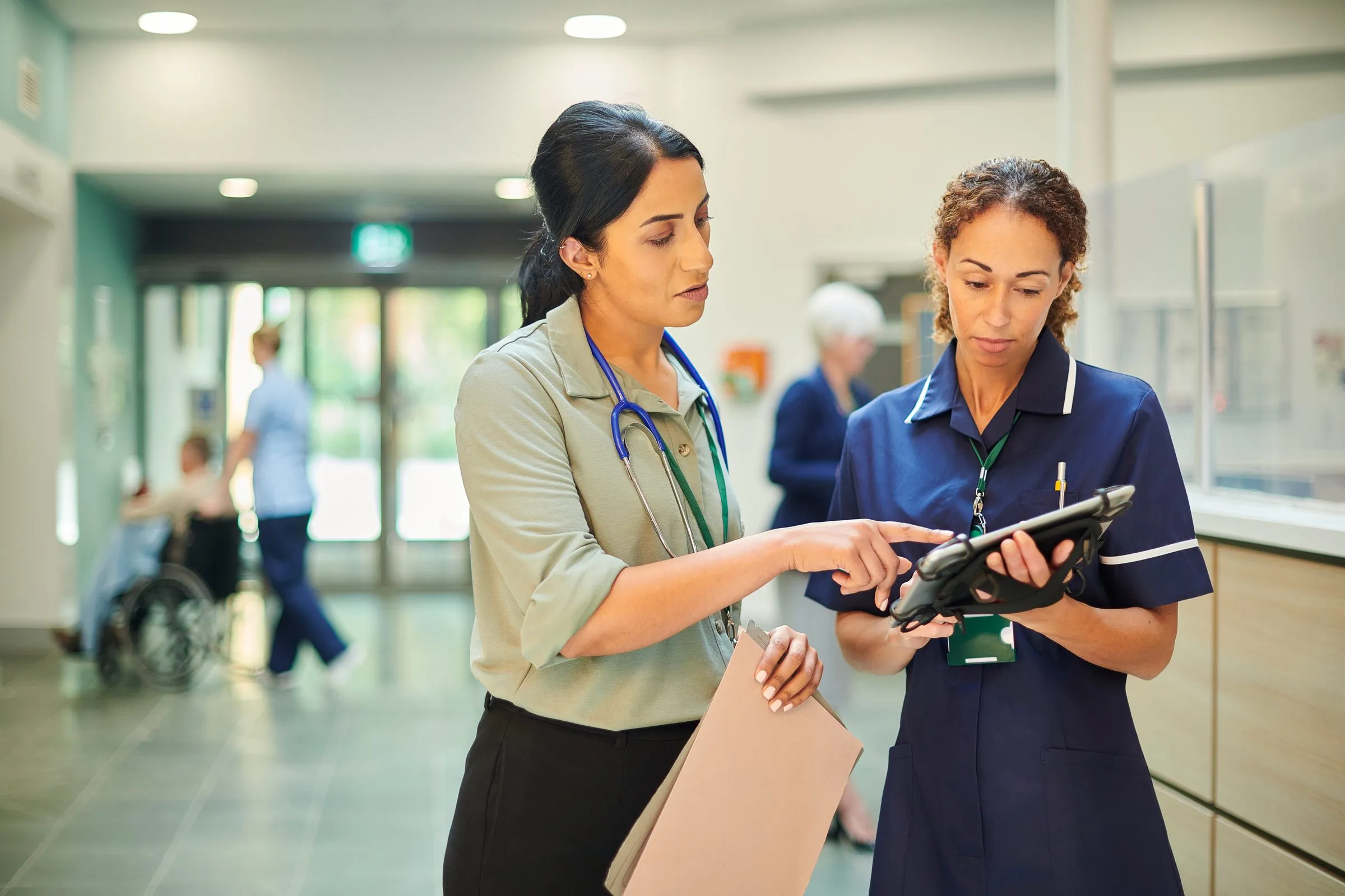 A doctor and a nurse look at a tablet together in a hospital corridor