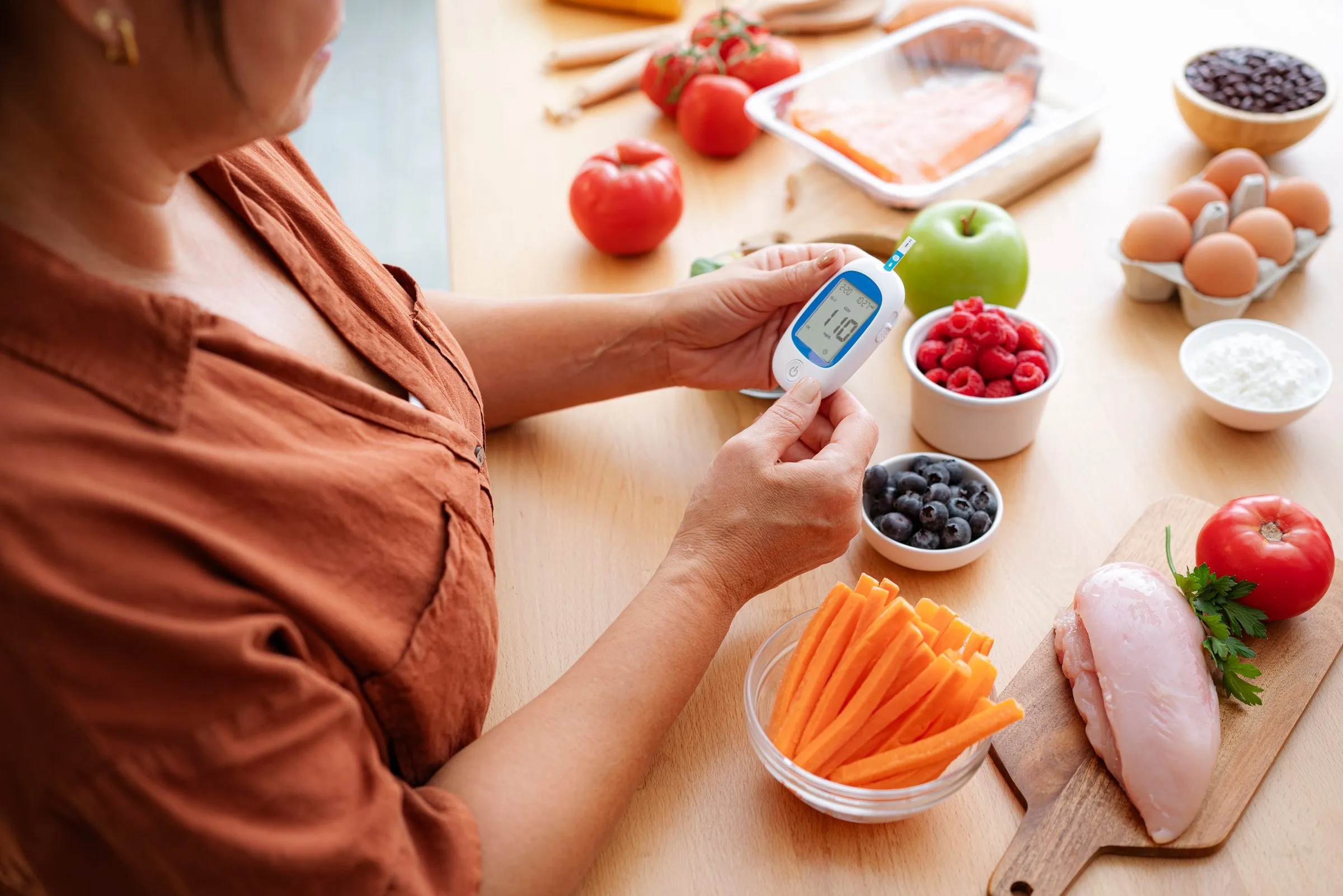 A woman reads her blood glucose meter beside healthy food on her kitchen table