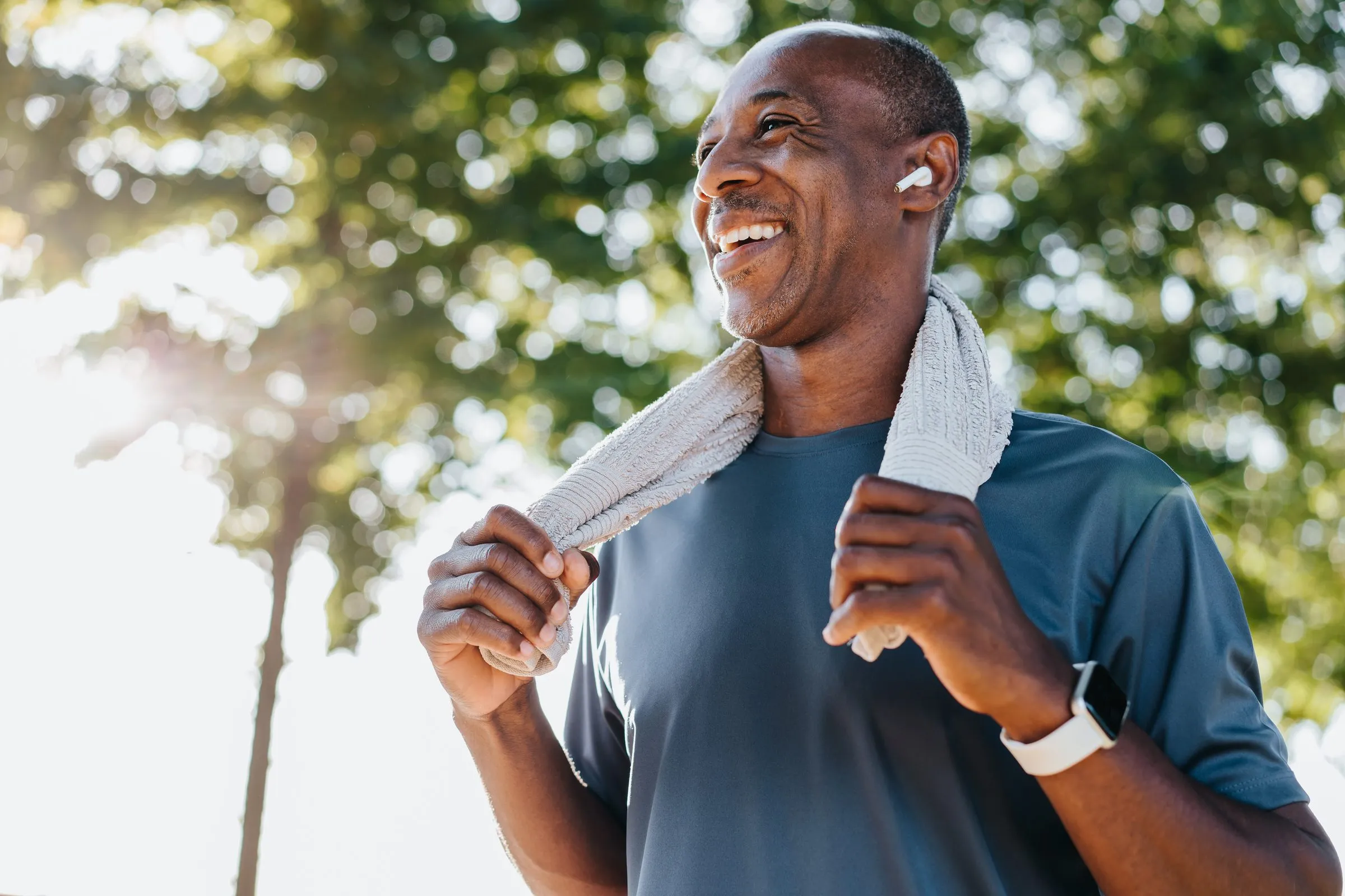 A man smiles after exercising outdoors, a towel round his neck