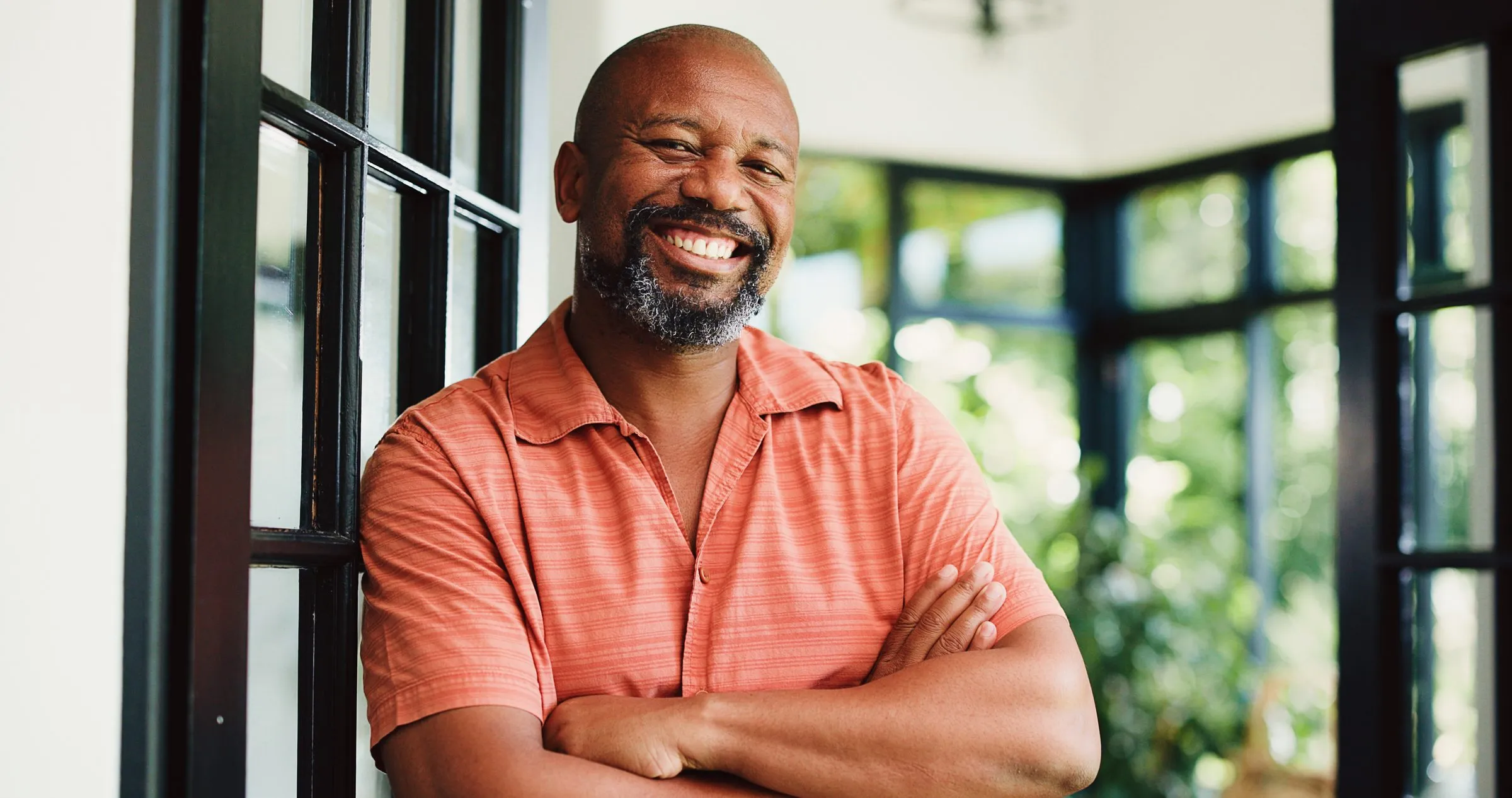 A smiling man stands at home with his arms crossed