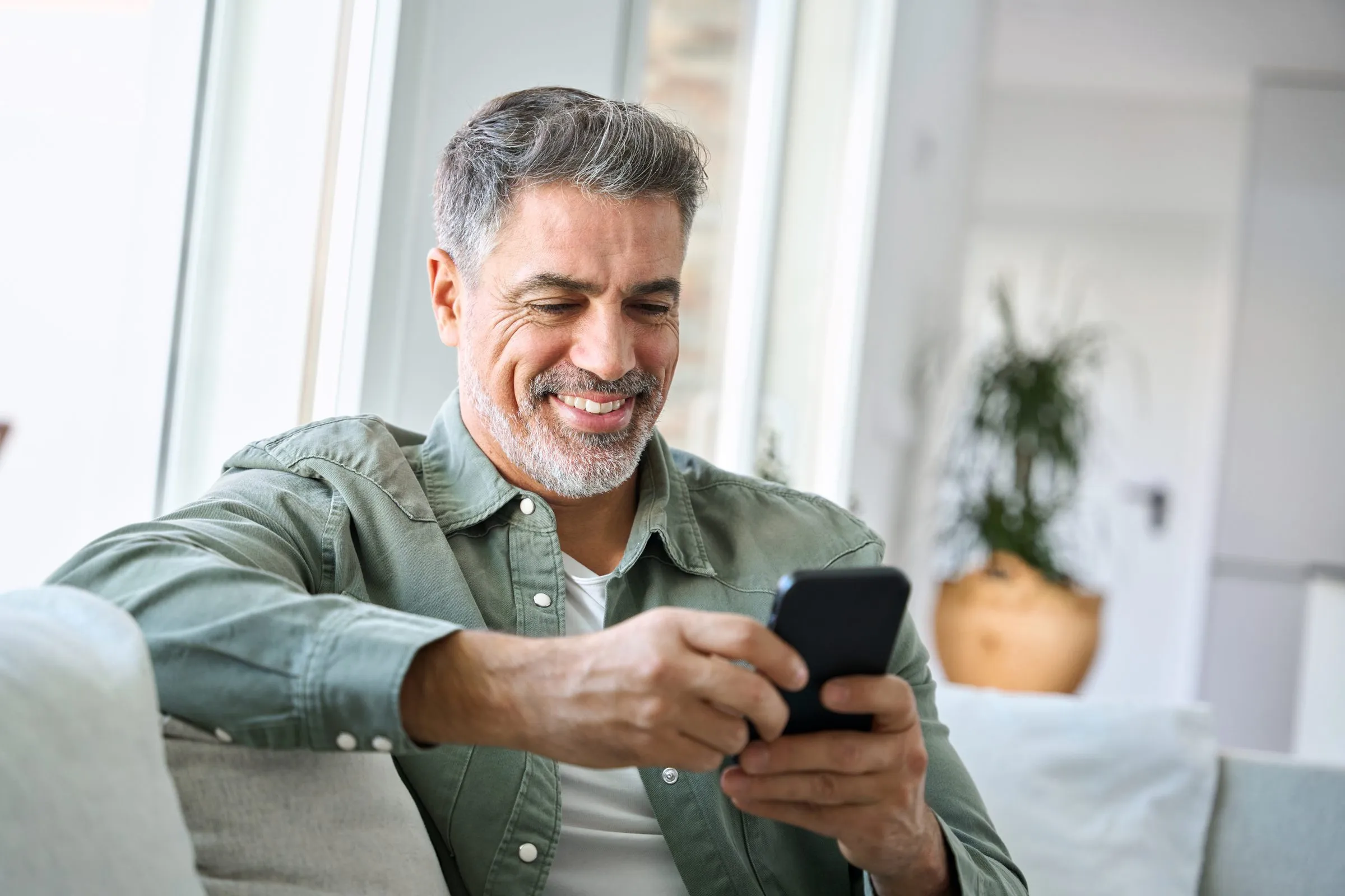 A man smiles at a message on his phone at home