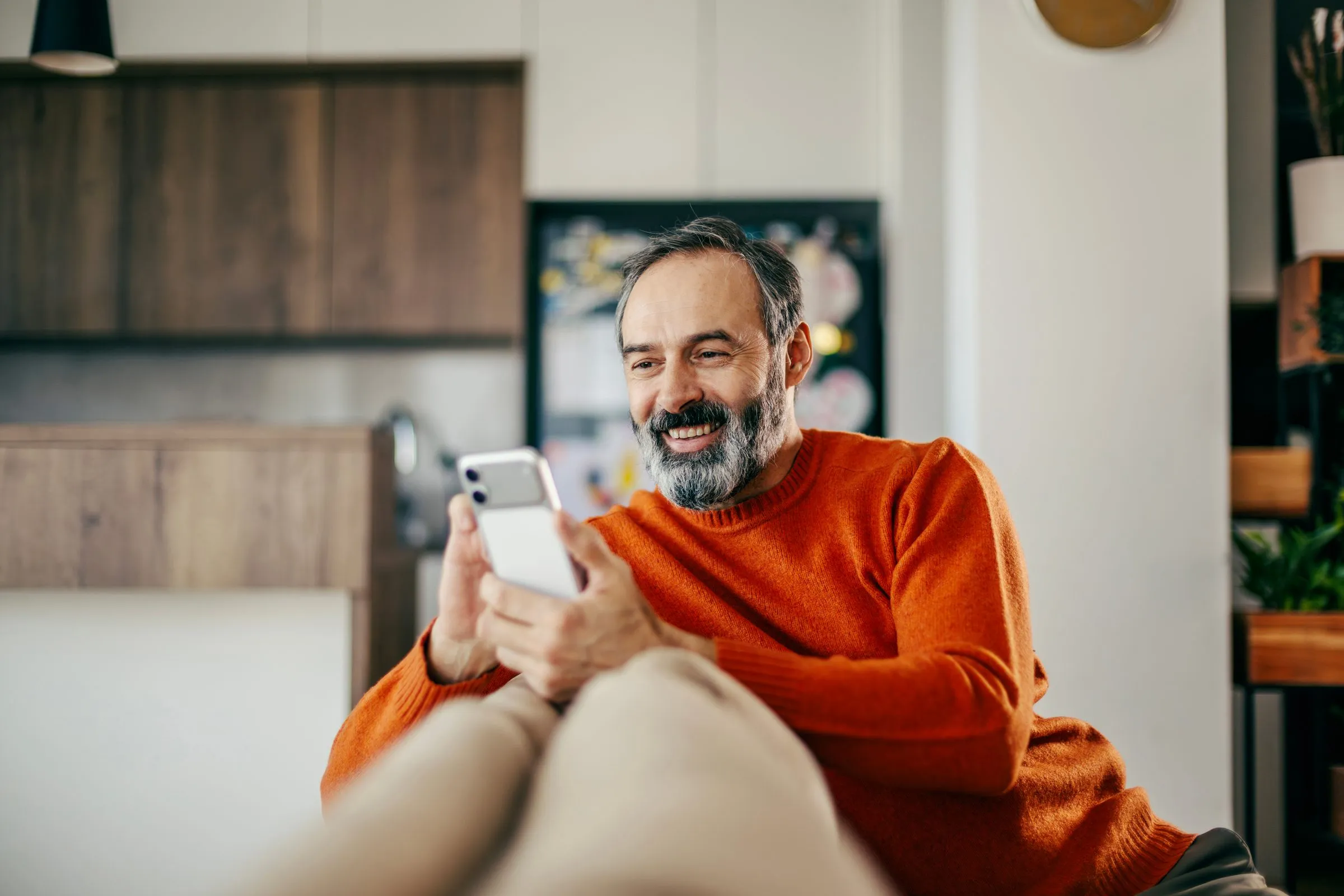 A man smiles at a text on his phone at home