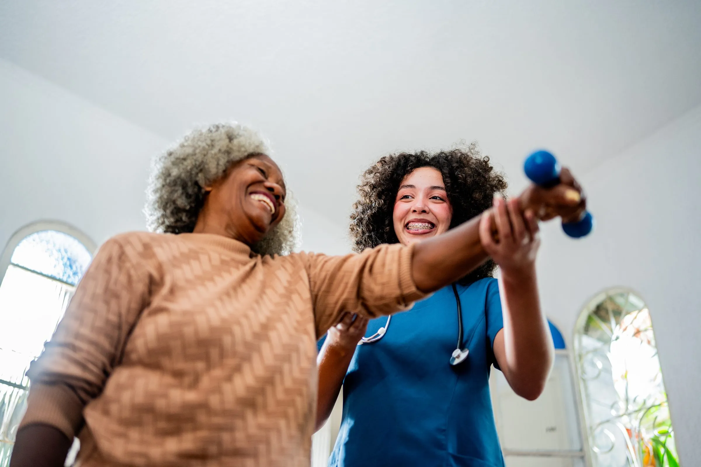 A physiotherapist helps an older woman exercise with hand weights