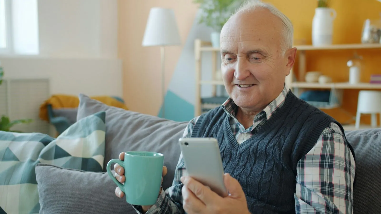 An older man smiles as he reads a message on his phone at home