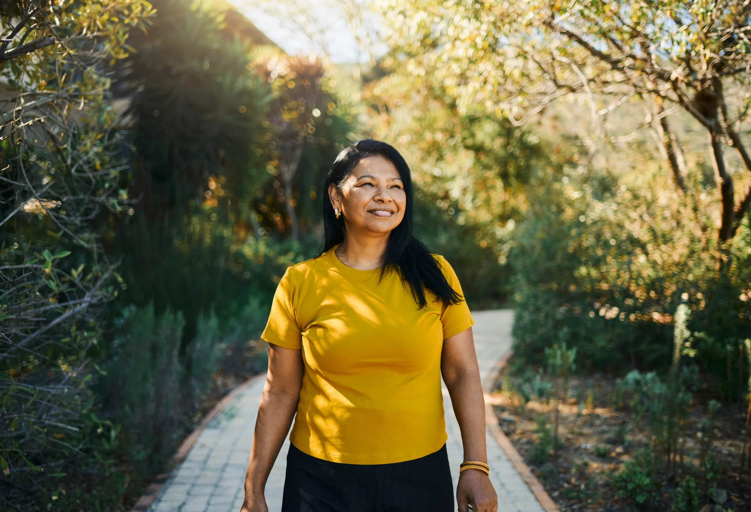 A woman smiles as she walks along a sunny garden path