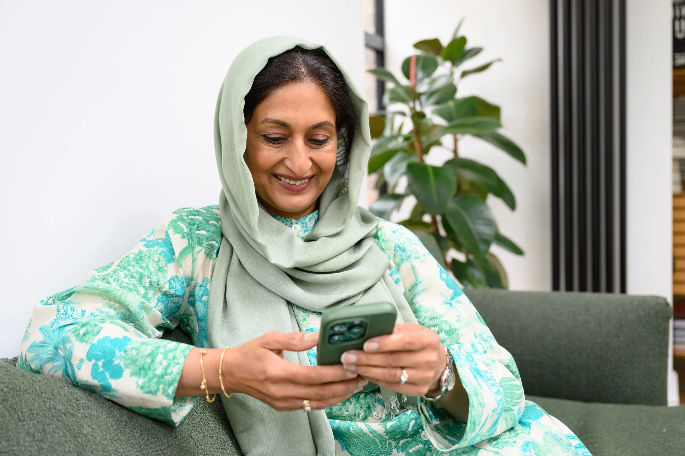 A woman in a headscarf smiles at her phone at home