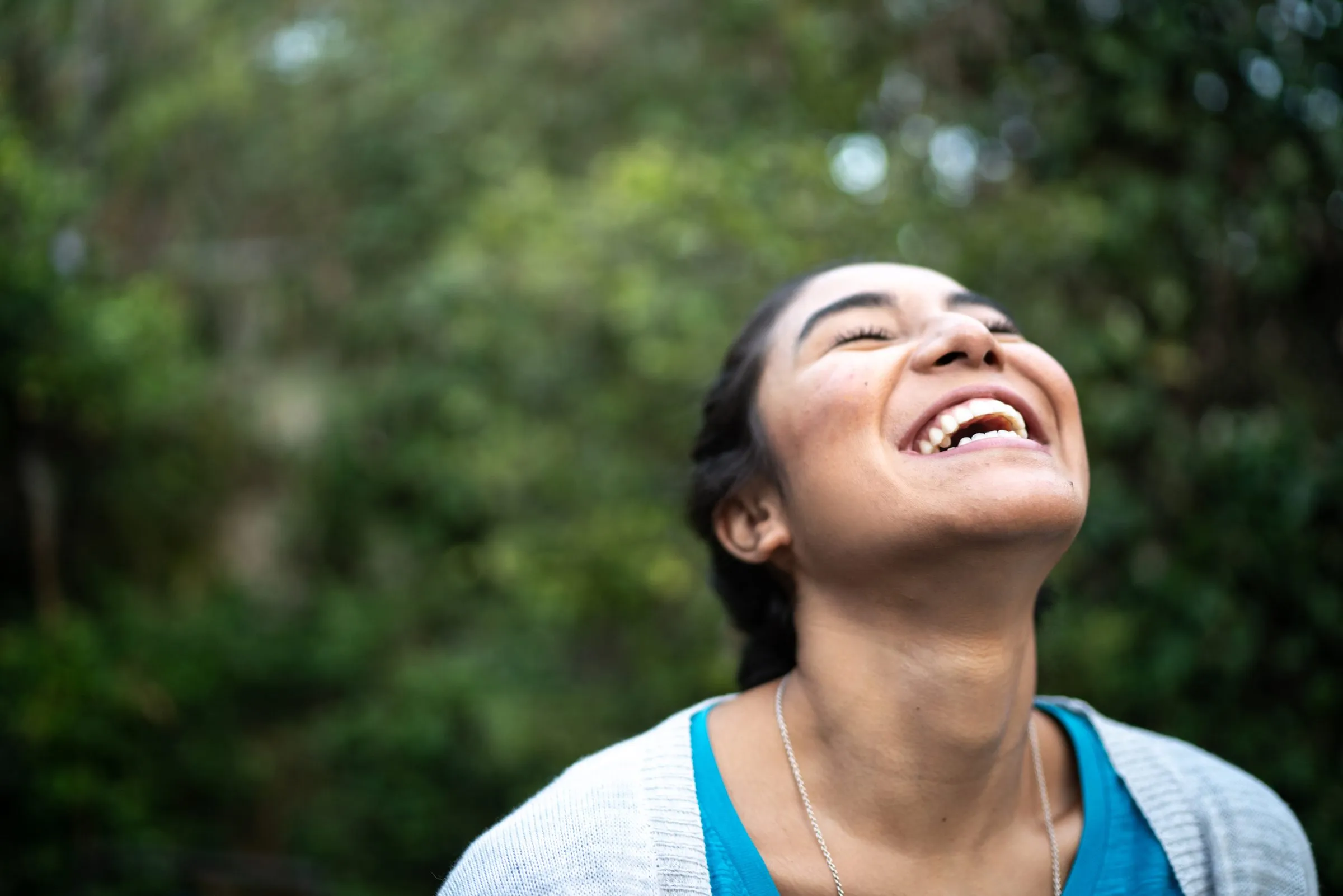 A young woman laughs outdoors, her head tipped back